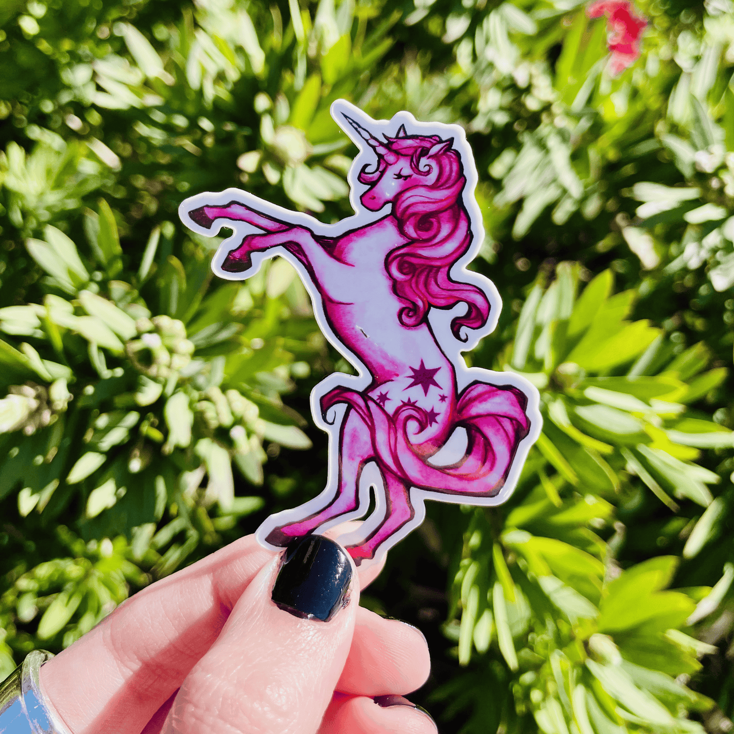 Pink unicorn sticker held in front of green foliage