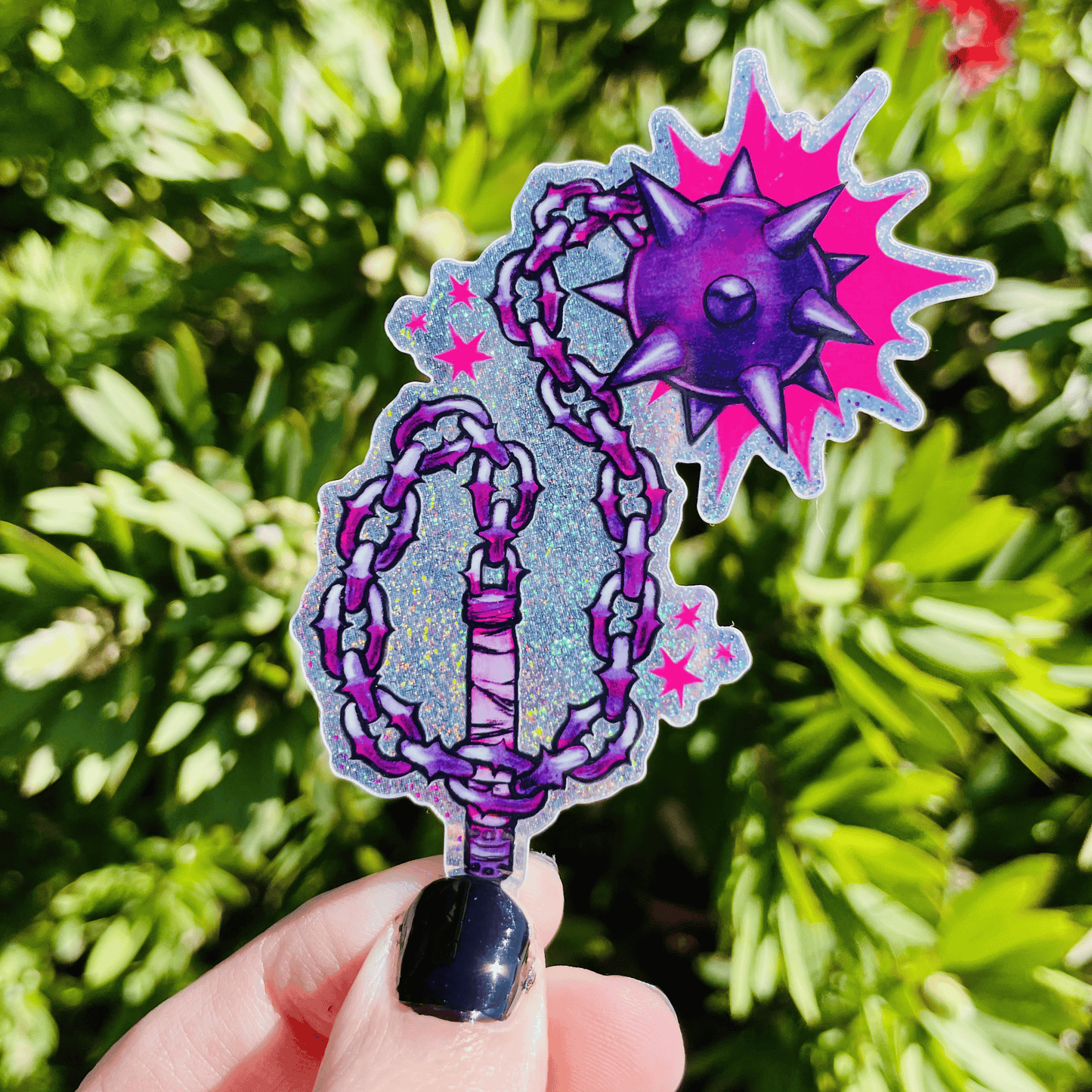 Decorative purple and pink flail held in front of green foliage